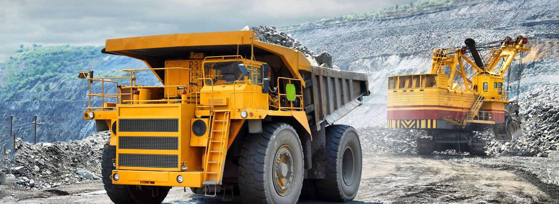 Grand camion minier jaune chargé de minerai avec une excavatrice imposante en arrière-plan dans une carrière à ciel ouvert.